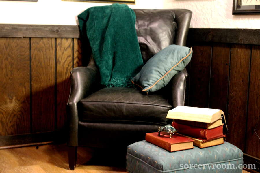 Balck leather chair with a green pillow and blanket, books and magnifying glass on a footstool