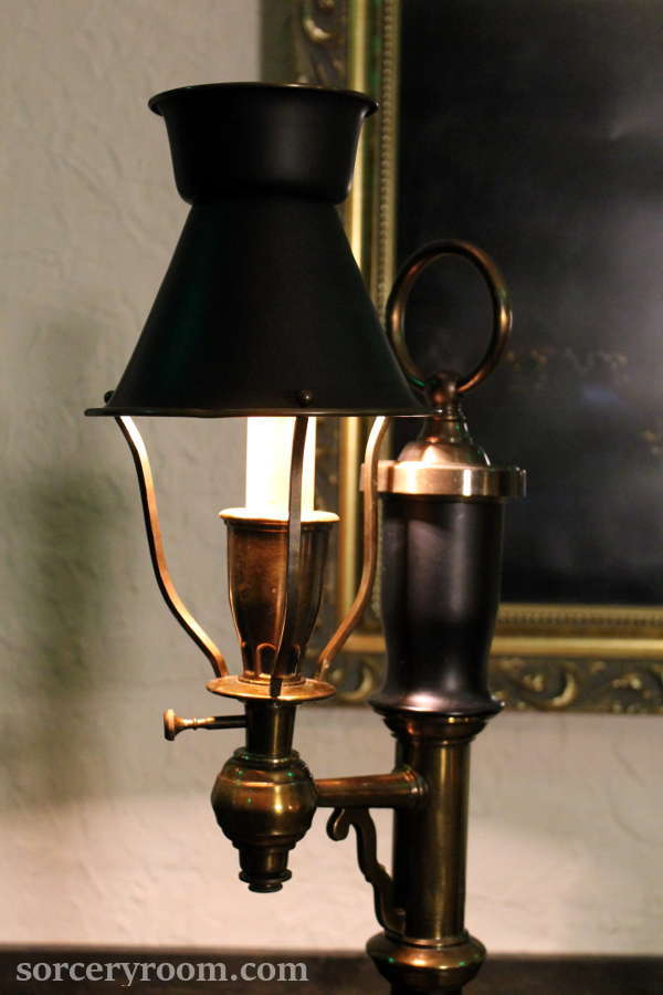 brass and black lamp with a metal shade, painting in the background