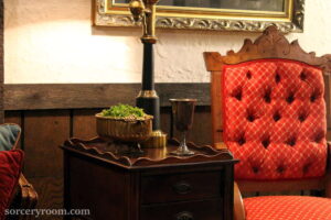 red upholstered chair, side table, brass vase with moss, silver goblet, lamp, gold frame