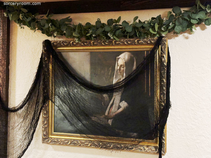 Harry Potter themed Halloween décor - a painting in a chick gilded frame with a black net over it and a Slytherin style garland hanging above