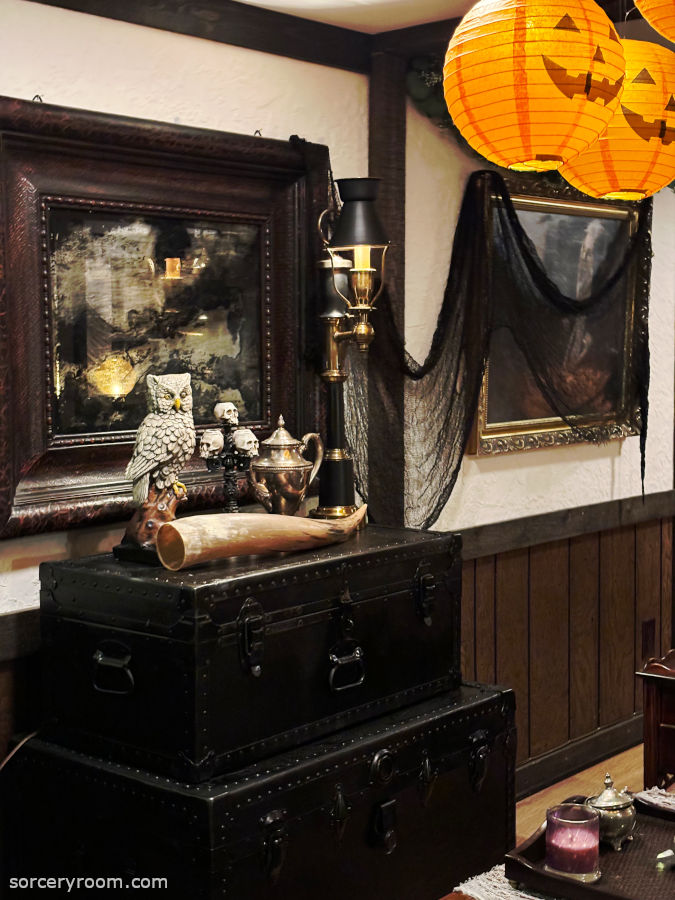 Harry Potter themed Halloween décor - dark and moody interior featuring black steamer trunks with sorcery themed decor on top, a large antiqued mirror above, decorated with Halloween netting and floating pumpkins