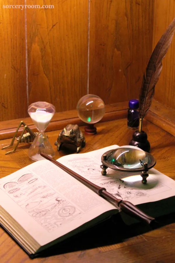 Harry Potter themed desk with an antique book, magic wand, magnifying glass, quill, crystal ball (divination orb).